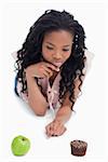 A young woman is choosing between an apple or a bun against a white background