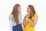 Two happy young women looking a smartphone against white background