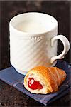 Mug of fresh milk and croissant with jam for breakfast.