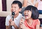 Family at home. Portrait of a happy Asian children singing karaoke through microphone in the living room