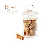 Cubes of brown  cane sugar in a glass pot on a white background.