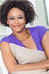 A beautiful mixed race African American girl or young woman looking happy and thoughtful holding a cushion