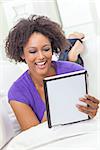 A beautiful happy mixed race African American girl or young woman laying down on sofa using a tablet computer