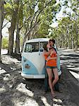 Young couple embracing leaning against front of camper van parked by road