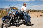 Senior man leaning on motorcycle on desert road