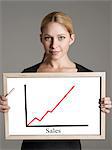 Portrait of young businesswoman showing sales graph against gray background