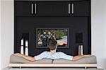 Back view of mid-adult man watching television in living room