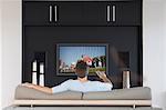 Back view of mid-adult man changing channels with television remote control in living room