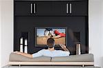 Back view of mid-adult man changing channels with television remote control in living room