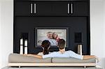 Back view of couple watching movie on television in living room
