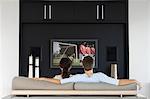 Back view of couple watching soccer game on television in living room
