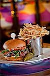 Beef Sirloin Burger with Smoked Bacon, Aged Goat Cheddar Cheese, Tomato Confit, Baby Arugula and Garlic Chive Aioli; Pickle and French Fries