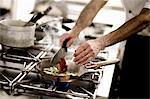 A chef adding chopped tomatoes to a pan of courgette