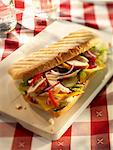 Chicken, onion, pepper, gherkins, cheese slices, lettuce and ketchup in a baguette on a wooden board