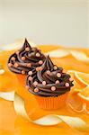 Two chocolate cupcakes with sugar confetti and oranges
