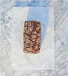 A tin-baked loaf topped with rolled oats, pumpkin seeds and sunflower seeds, on paper, on a marble slab dusted with flour