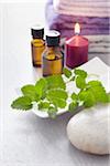 Sprig of lemon balm, fresh herbs, candle, towel and bottles of essential oil for aromatherapy