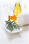 Sprig of rosemary and a towel with bottles of aromatic oil for aromatherapy