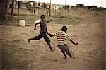 Two young black boys play soccer together in the rural streets