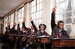 A group of students in a classroom raise their hands to answer a question