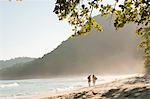 Brazil, Rio de Janeiro State, Costa Verde, Green coast,, Paraty, a couple with a surf board and a guitar walking along Praia do Sono beach near Trindade