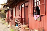 South America, Brazil, Sao Paulo, Santo Andre, Paranapiacaba, a woman looks out of a window in an English built wooden house in the railway village of Paranapiacaba set in the Atlantic Coastal rainforest near on Sao Paulos city limits