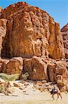 Chad, Elikeo, Ennedi, Sahara. A Toubou tribesman on his camel is dwarfed by the massive weathered sandstone rocks at Elikeo.