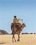 Chad, Bechike, Ennedi, Sahara. A Toubou nomad riding a camel near Bechike.