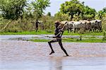 A young Dassanech herdsboy runs across shallow water beside the Omo River. The river bursts its banks annually during heavy rain in the Ethiopian Highlands, Ethiopia