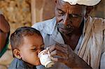 India, Rajasthan, Ajabgarh. A village man helps a child drink tea.