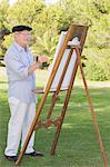 Old man painting outside using an easel