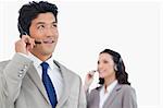 Call center agent with headset and colleague behind him against a white background