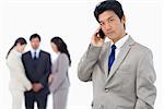 Serious businessman on cellphone with team behind him against a white background