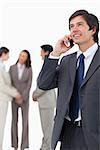 Salesman talking on mobile phone with team behind him against a white background