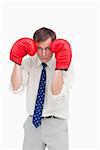 Businessman with boxing gloves taking cover against a white background