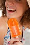 Orange ice lolly held by a smiling young woman in bikini