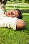 Man lying in grass with his eyes closed and his hands resting underneath the side of his head