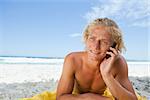 Blonde man lying on his beach towel while talking on his mobile phone