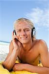 Young blonde man attentively listening to music while lying on then beach