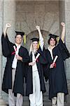 Happy graduates raising arm with university in backgroung