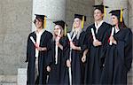 Smiling graduates posing while holding their diploma in front of the university