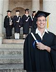 Close-up of a blue eyes graduate smiling with her friends in background in front of the university