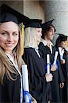 Portrait of a blonde graduate with blue eyes next to her friends posing