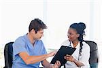 Young serious doctor showing something on a clipboard to his smiling co-worker