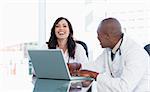 Young nurse laughing while working on a laptop with a relaxed co-worker