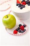 Apple and bowl of berries cream and  a tape measure against a white background