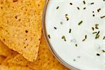 Close up of a bowl of white dip with herbs  beside nachos