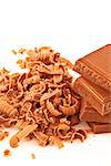 Many chocolate shavings beside a pile of chocolate against a white background