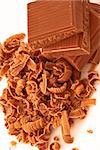 Close up of pile of chocolate pieces and chocolate shavings against a white background