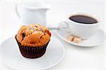 Muffin and a cup of coffee on white plates with sugar and milk against a white background